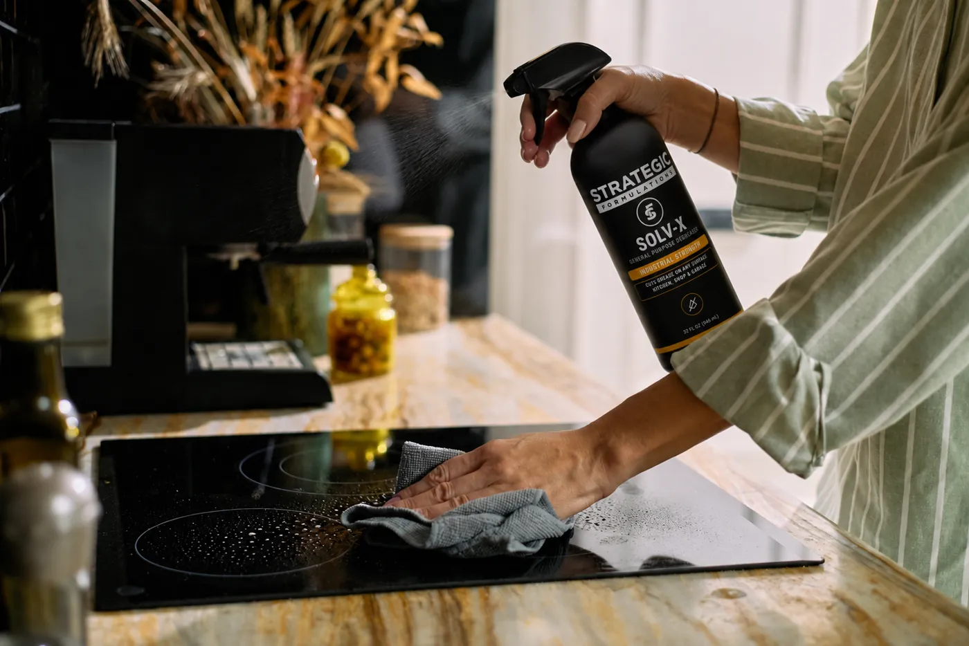 Wiping a splattered induction cooktop clean with SOLV-X in a home kitchen